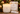 A lit double-wick soy candle in a frosted white glass jar sits beside its decorative white and gold LINNEA JULETIDE box, with a matchbox and holiday ornaments in the background.