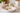 A white ceramic serving bowl with a scalloped rim, decorated with a hand-painted botanical pattern of green leaves, red berries, and yellow accents, set on a marble countertop in a kitchen.