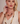 A blonde woman wearing a matching jewelry set with chunky gold and cream-colored chain necklaces, matching drop earrings, and a bracelet, styled with a cream-colored sleeveless top against a soft beige background.