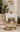 A decorative hanging ornament featuring a nativity scene with a baby in a manger, displayed on a gold-toned metal stand against a softly blurred indoor background.