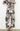 A model wearing a matching two-piece set featuring a wide-leg pants and a short-sleeve top, both with an abstract floral pattern in gray, burgundy, and black on a light beige background.