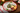 A scalloped ceramic Christmas-themed serving platter with a red rim, decorated with a central Christmas tree, holly, stars, and gold dots, styled with crackers, cheese, cranberries, and walnuts on a wooden table.