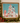 Framed Christmas art print featuring a decorated tree, pink poodle, Dalmatian, and other dogs in a snowy winter scene, displayed on a mantel with holiday greenery and wrapped gifts.