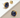 A pair of gold stud earrings with cushion-cut dark blue faceted gemstones, shown on a clean white and beige diagonal background. One earring is displayed in front, and the other is shown from the back with its screw-back fastener visible.