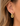 A close-up of a model's ear wearing a gold huggie hoop earring with a dangling rectangular link charm.