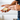 A close-up of a person's hands holding an open silver tin of balm or lip balm, with the other hand reaching toward the product. The person is wearing a silver ring on their left hand.