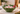 A green ceramic bowl with a leaf-like scalloped rim, filled with red-and-white peppermint candies and red berries, set on a marble countertop in a holiday-themed interior.