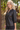 A woman with blonde hair wearing a black faux-leather button-up blouse with puff sleeves, standing outdoors in a garden setting.