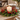 A lit white pillar candle placed in a green evergreen wreath with red berries on a wooden dining table, with plates and a chair blurred in the background.
