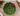 A green ceramic bowl shaped like a holly leaf with red berries, set on a marble surface with holiday decorations in the corner.