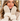 A close-up lifestyle shot of a woman wearing cream-colored faux fur and suede mittens with a small gold embroidered monogram logo, paired with a beige knit sweater.