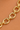 A close-up of a shiny gold chain with elongated oval links, laid diagonally across a warm peach-colored textured surface.