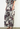 A model wearing wide-leg cropped pants with a gray, white, and burgundy floral pattern, paired with a matching top and black strappy heels, standing against a plain white wall.