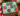 A completed jigsaw puzzle featuring 12 decorated donuts with Christmas themes, displayed on a wooden table surrounded by holiday decorations like gingerbread cookies, pine branches, and a mug of marshmallows.
