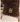 A close-up of a brown fuzzy knit cuff with a gold embroidered monogram logo, worn over a cream ribbed sweater.