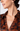 Close-up of a woman wearing a satin-like collared blouse with a dark brown and black floral pattern, paired with gold hoop earrings against a light gray background.