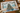 A completed jigsaw puzzle featuring a coastal Christmas scene with a decorated tree, beach, sailboat, and gift boxes, styled on a wooden tabletop with holiday decor.
