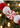 A close-up of a festive holiday garland featuring red and white felt pom-poms and a glittery red-and-white peppermint candy ornament, set against a blurred Christmas tree background with warm bokeh lights.