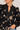 A close-up of a woman wearing a black long-sleeve blouse with beige floral embroidery and a split neckline, paired with light blue jeans.