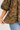 Close-up of a woman wearing a sheer olive green floral puff-sleeve top with blue jeans, holding the hem to show the fabric's flow and texture.