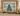 A framed coastal Christmas art print hangs on a wall above a mantel decorated with a lit green garland, candles, starfish, and beach-themed ornaments. The artwork shows a decorated Christmas tree by the ocean with the text 'Coastal Christmas' at the top.