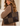 A woman wearing a brown knit sweater carries a large patchwork leather tote bag in dark brown and taupe. The bag features a checkerboard pattern of smooth and suede-like panels, with a small gold 'SARA LLOYD' logo on the bottom right corner.