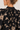 Close-up of a woman wearing a black blouse with beige floral embroidery and a striped high collar, shown from the back over her shoulder.
