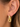 A close-up of a person's ear wearing a polished gold huggie hoop earring with a dangling open-link charm.