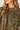Close-up of a woman wearing an olive green short-sleeve blouse with a dense multicolor floral and butterfly print, featuring a smocked neckline.