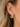 A close-up of a woman's ear wearing a gold hoop earring adorned with clear round gemstones.