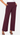 A person wearing a pair of wide-leg cropped pants in a deep burgundy or plum tone, paired with a white top and black strappy heels, against a light gray studio background.