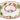 A white ceramic holiday serving platter with a scalloped edge, featuring a red rim and a printed wreath pattern of green holly leaves, red berries, and light blue accents.