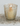 A lit cream-colored candle inside a clear glass votive holder decorated with a pattern of gold dots, set on a textured stone surface against a neutral light gray background.