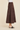 A model wearing a dark brown tiered faux-suede midi skirt with a white top and black mule sandals, shown from the waist down against a solid beige background.