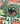 A close-up of a colorful jigsaw puzzle featuring a circular green emblem with a vintage film camera and the words 'CLASSIC CHRISTMAS MOVIES.' The surrounding puzzle design includes holiday houses, trees, roads, and vehicles in a festive illustrated style.