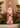 A distressed red and white Santa Claus figurine standing on a mantel, surrounded by green pine garland, red berries, and brass candlesticks in a warm indoor setting.