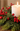A lit white pillar candle surrounded by green evergreen branches and clusters of bright red berries on a wooden surface.
