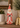 A distressed red and white Santa Claus figurine standing on a wooden shelf, flanked by potted greenery and a gold bell.
