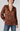 A woman wearing a long-sleeve satin button-up blouse with a rust-brown and black floral pattern, paired with blue jeans, against a light gray studio background.
