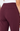 Close-up rear view of a person wearing high-waisted burgundy pants with a white top visible at the waist.