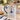A white ceramic mug with a blue handle and blue decorative print of a ballerina, set on a marble countertop in a cozy kitchen scene with a croissant, flowers, and a candle.