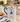 A white ceramic mug with a blue handle and blue decorative print of a ballerina, set on a marble countertop in a cozy kitchen scene with a croissant, flowers, and a candle.