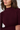 Close-up of a woman wearing a ribbed mock neck sweater in deep burgundy, showing the texture of the knit fabric and her hair against a light gray background.