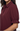 A close-up of a woman wearing a short-sleeve button-front blouse in deep burgundy with a pointed collar and gathered ruffled cuffs.