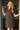A smiling blonde woman stands in a doorway wearing a short-sleeve collared button-front dress with an allover brown floral print on a dark navy background.
