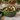 A green ceramic salad bowl filled with mixed greens, pecans, blue cheese, cranberries, and a pear slice, set on a marble table with a napkin and fork.