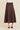A brown suede-like A-line midi skirt with horizontal seam detailing, shown on a model from the waist down wearing a white top and black heeled sandals against a beige background.