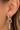 A close-up of a person's ear wearing a multi-layered hoop earring. The earring features a gold-toned ring, a silver-toned textured ring, a larger silver-toned hoop, and a dangling silver-toned bar with a small top loop.