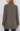 A woman shown from the back wearing a brown and beige tweed blazer with a subtle plaid pattern, paired with black pants, against a light gray studio background.